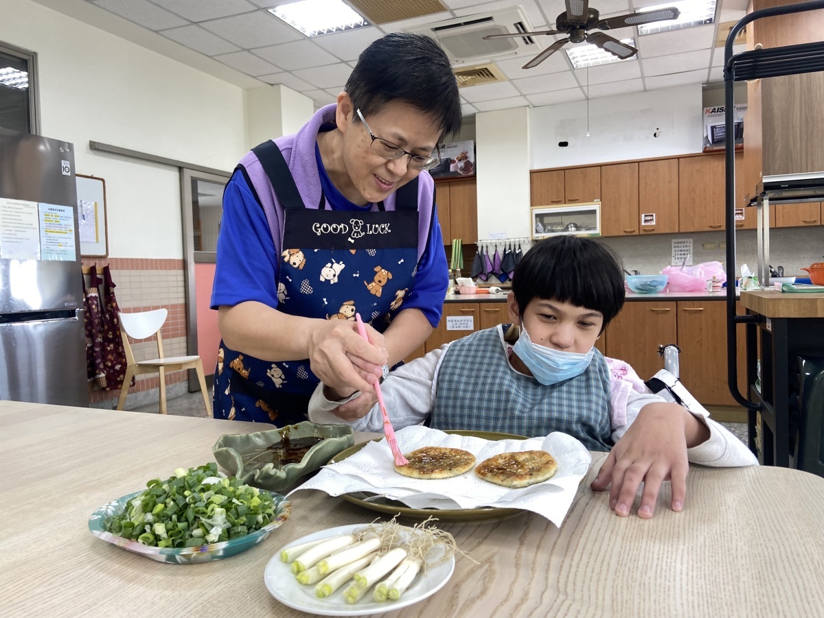 揭金鳳6.(陶藝課)結合陶藝技法協助國小部學生於自己完成的蔥油餅上面,運用刷子刷醬油膏的動作。